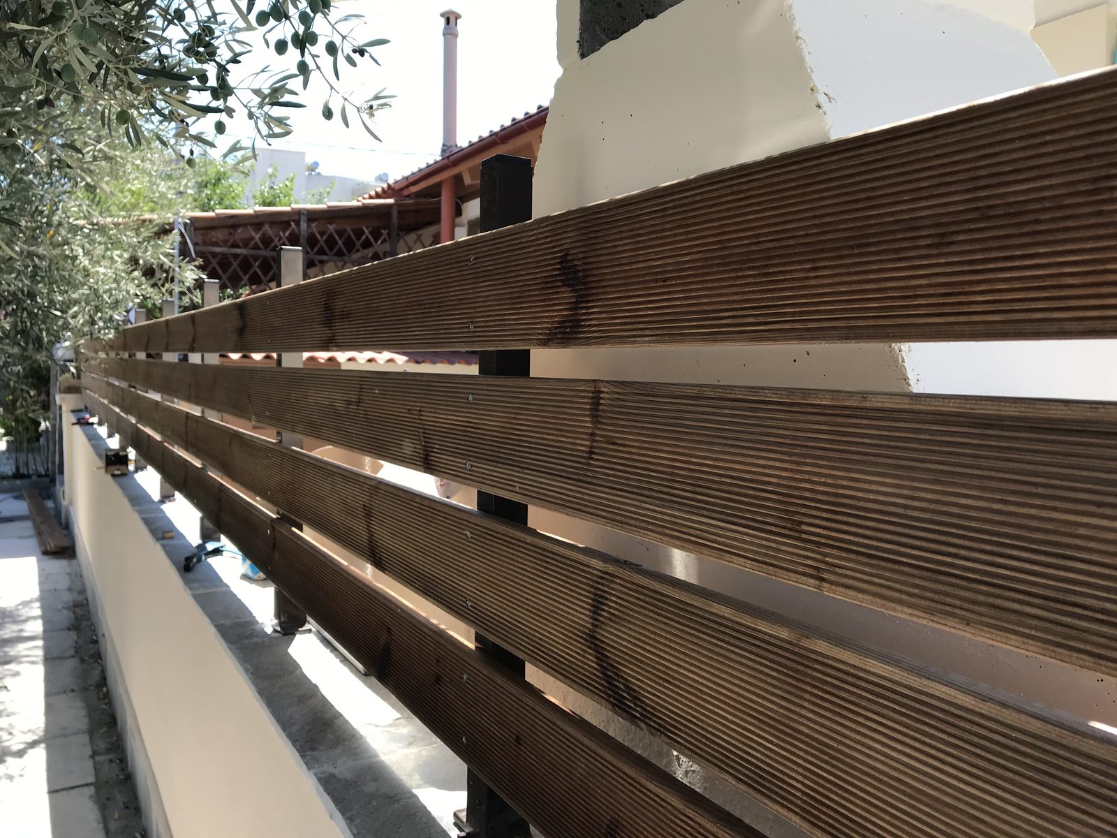 Οριζόντιες τάβλες από σουηδικό ξύλο εμποτισμού σε μεταλλικό σκελετό, πάνω σε μαντρότοιχο